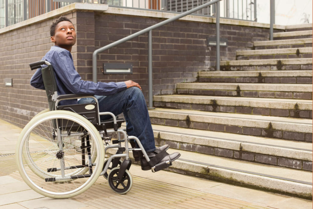 Young man in a wheelchair alone at the bottom of a staircase.